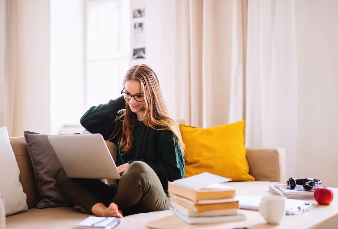 Young female student sitting on a sofa and using a laptop while studying.