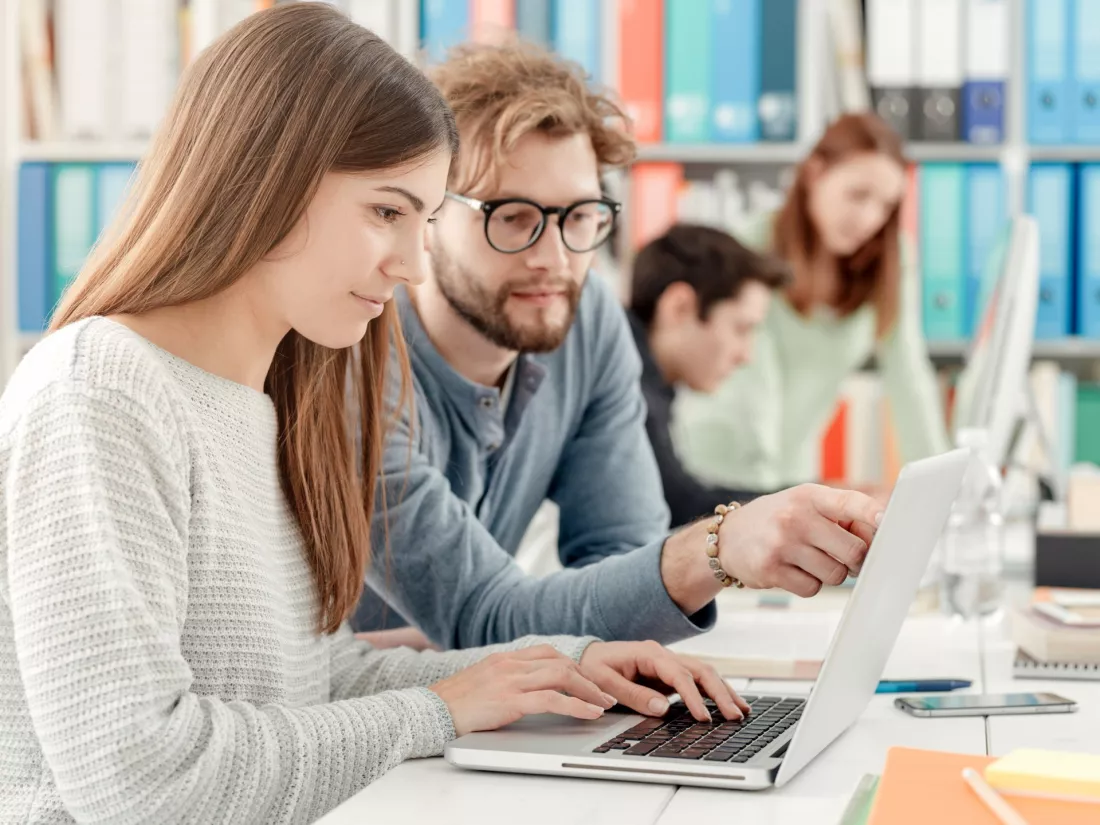 Studenci pracują razem przy laptopie w sali z regałami